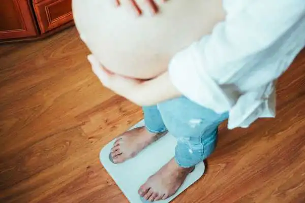 Image of woman weighing herself and experiencing weight gain through pregnancy Wales